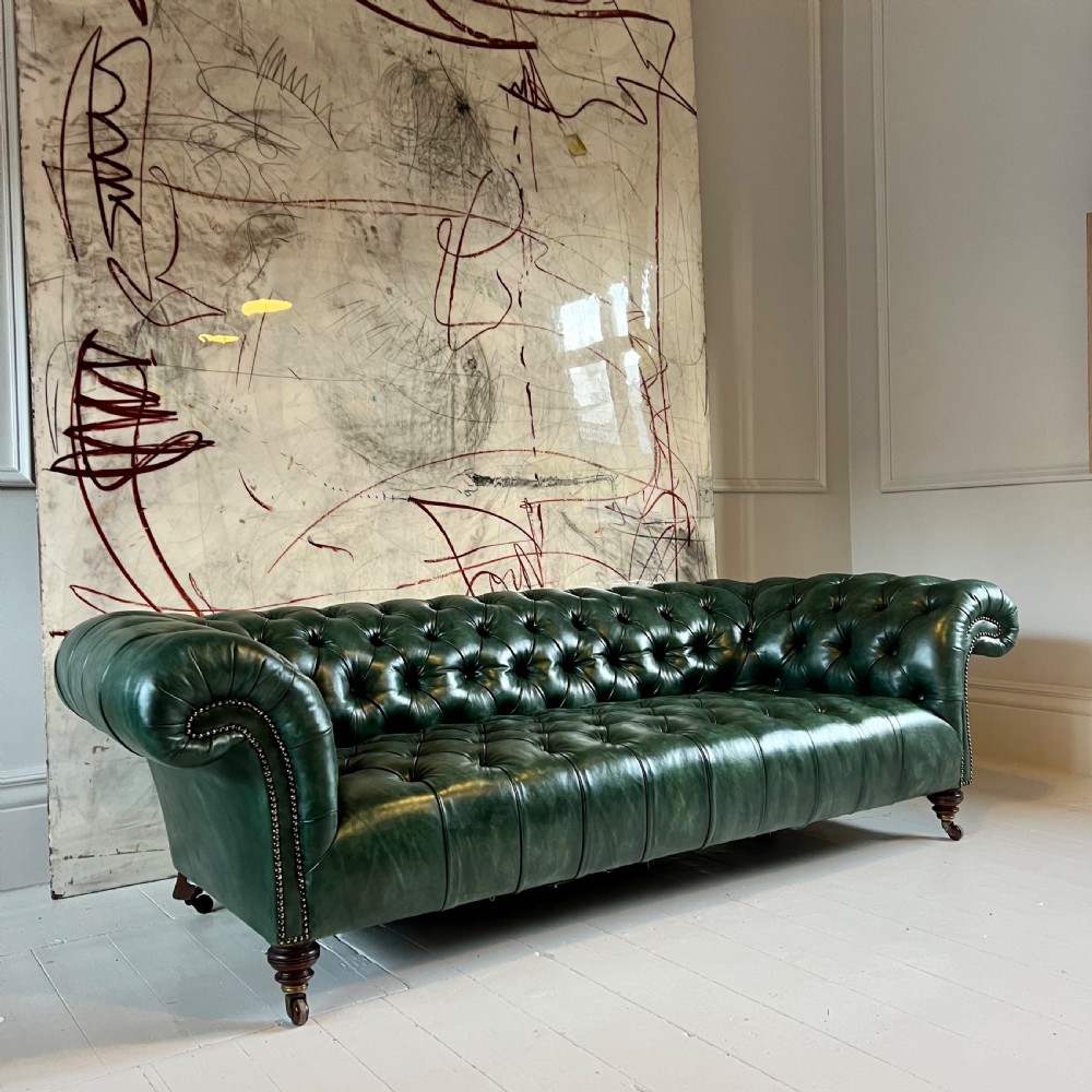 A nineteenth-century green leather Chesterfield sofa featuring deep button tufting, rolled arms with brass nailhead trim, and turned mahogany legs on brass castors. View VI