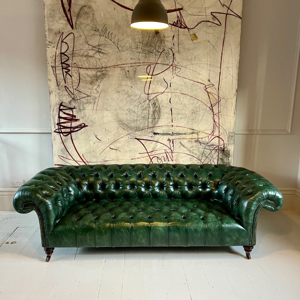 A nineteenth-century green leather Chesterfield sofa featuring deep button tufting, rolled arms with brass nailhead trim, and turned mahogany legs on brass castors. View VII