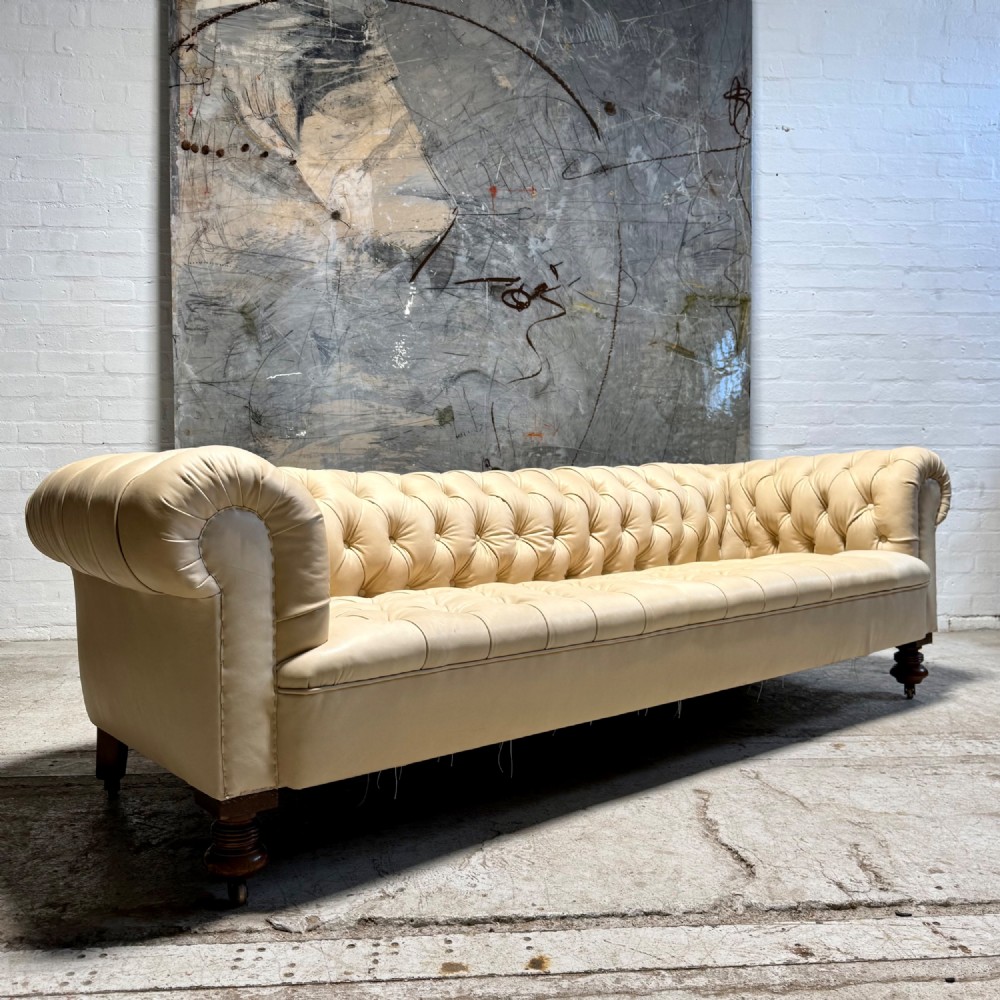 An antique Edwardian four-seater Chesterfield sofa upholstered in natural undyed cream leather with deep buttoning and turned wooden legs.
