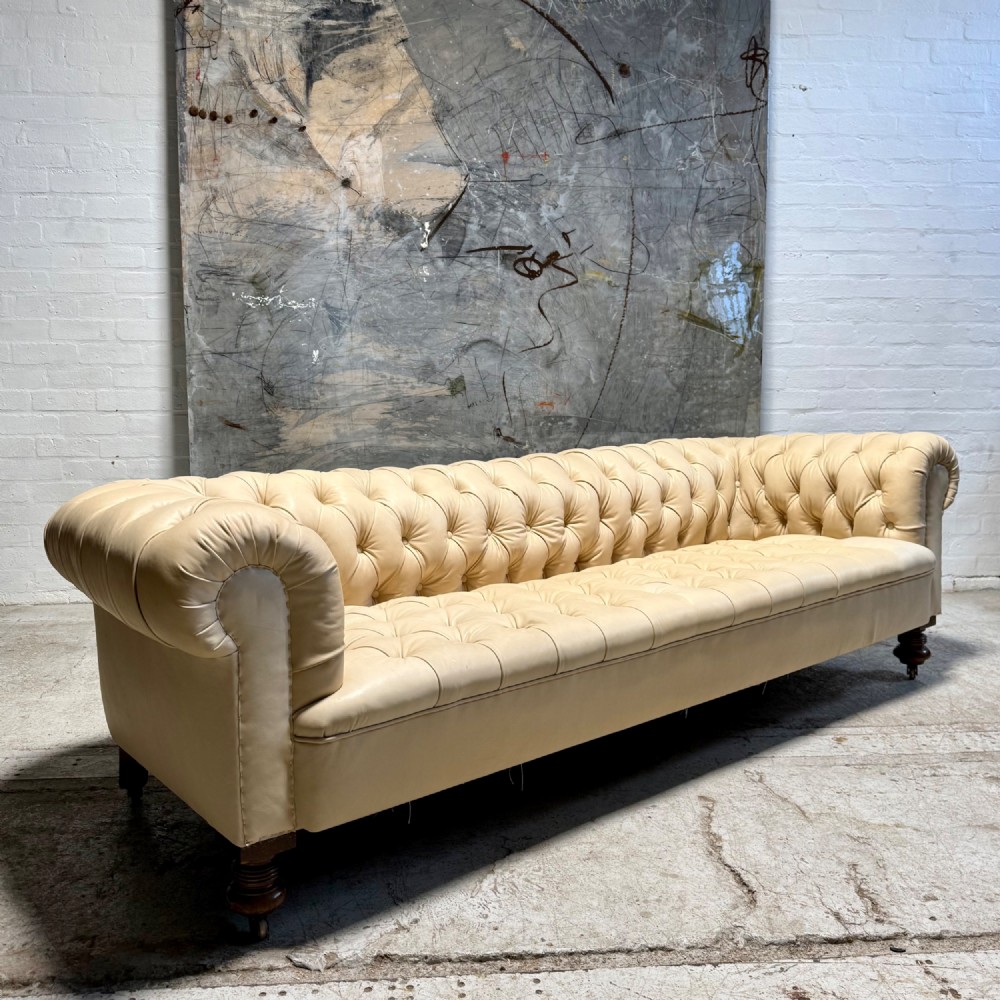 An antique Edwardian four-seater Chesterfield sofa upholstered in natural undyed cream leather with deep buttoning and turned wooden legs. View II
