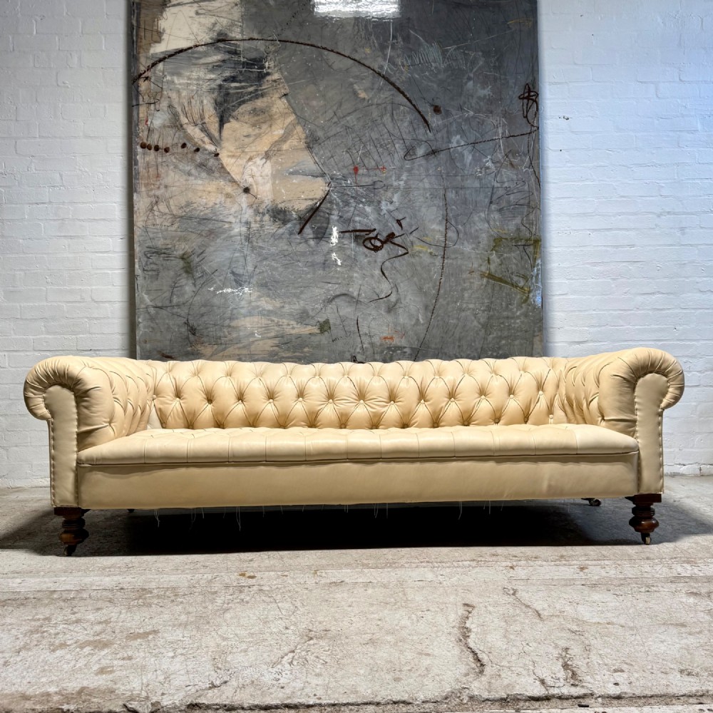 An antique Edwardian four-seater Chesterfield sofa upholstered in natural undyed cream leather with deep buttoning and turned wooden legs. View III