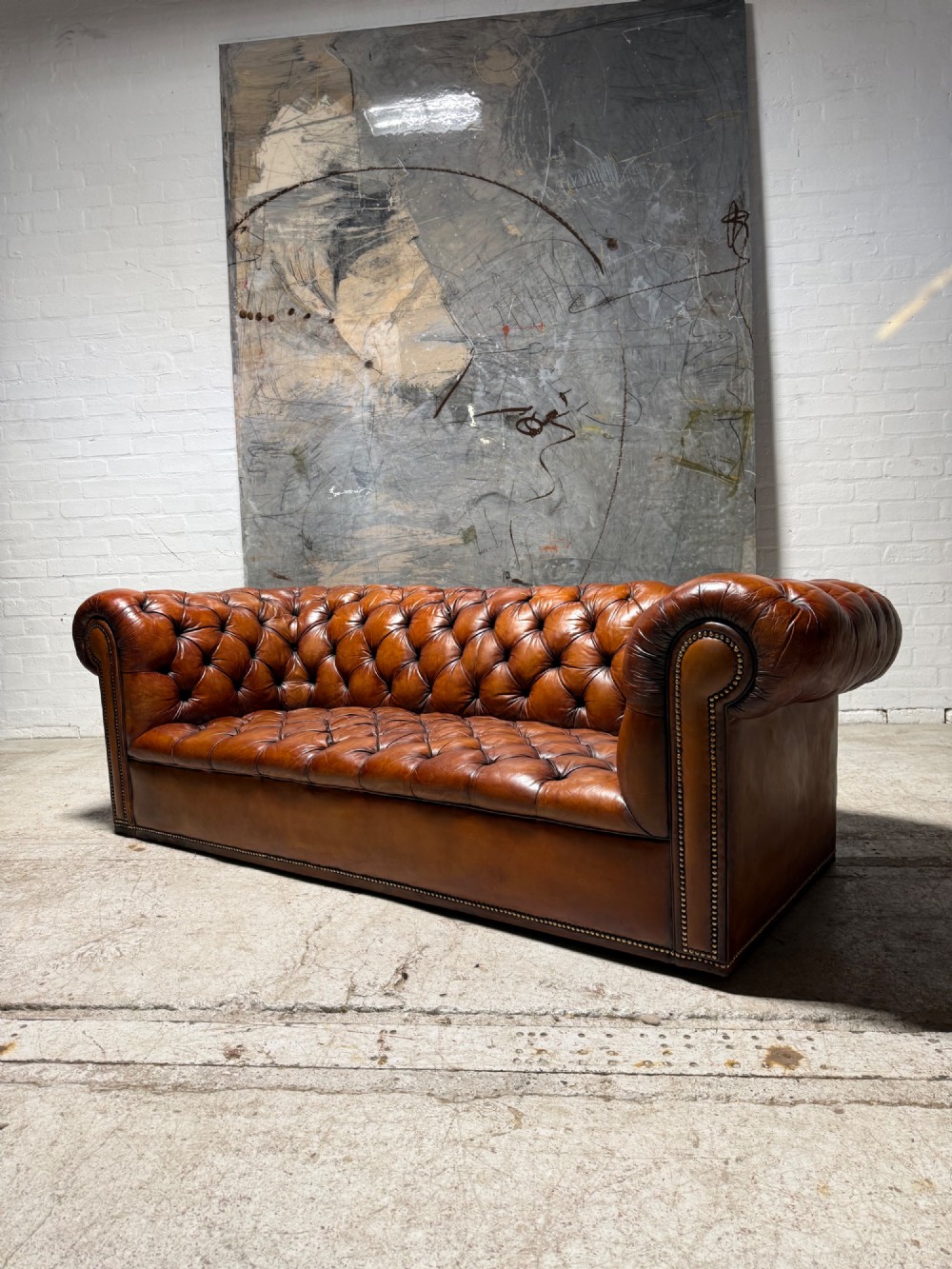 An early twentieth-century three-seater leather Chesterfield sofa with deep-buttoned tufted upholstery, rolled arms, and brass studding detail. View II