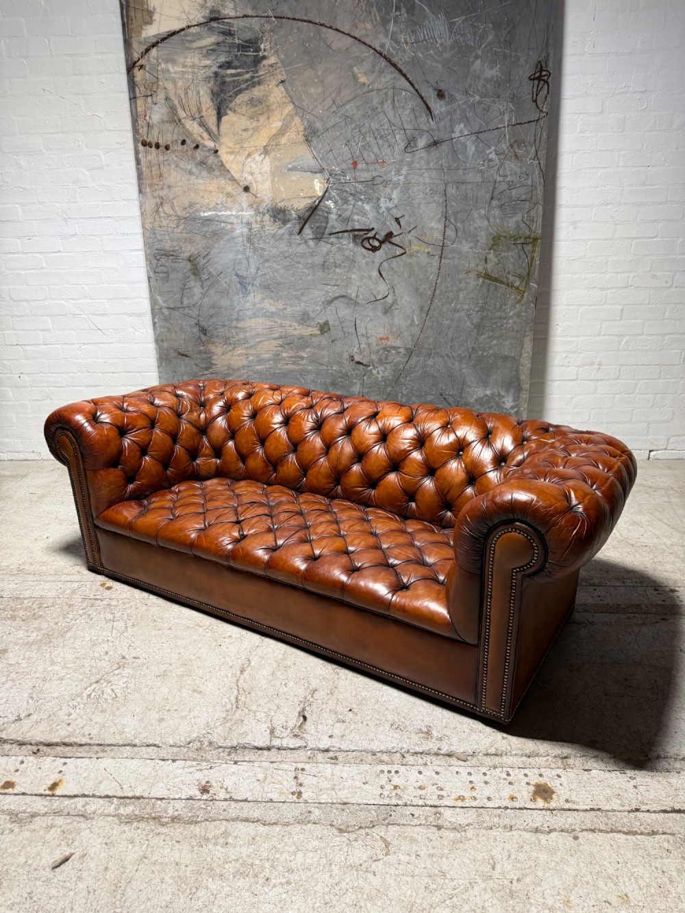 An early twentieth-century three-seater leather Chesterfield sofa with deep-buttoned tufted upholstery, rolled arms, and brass studding detail. View III