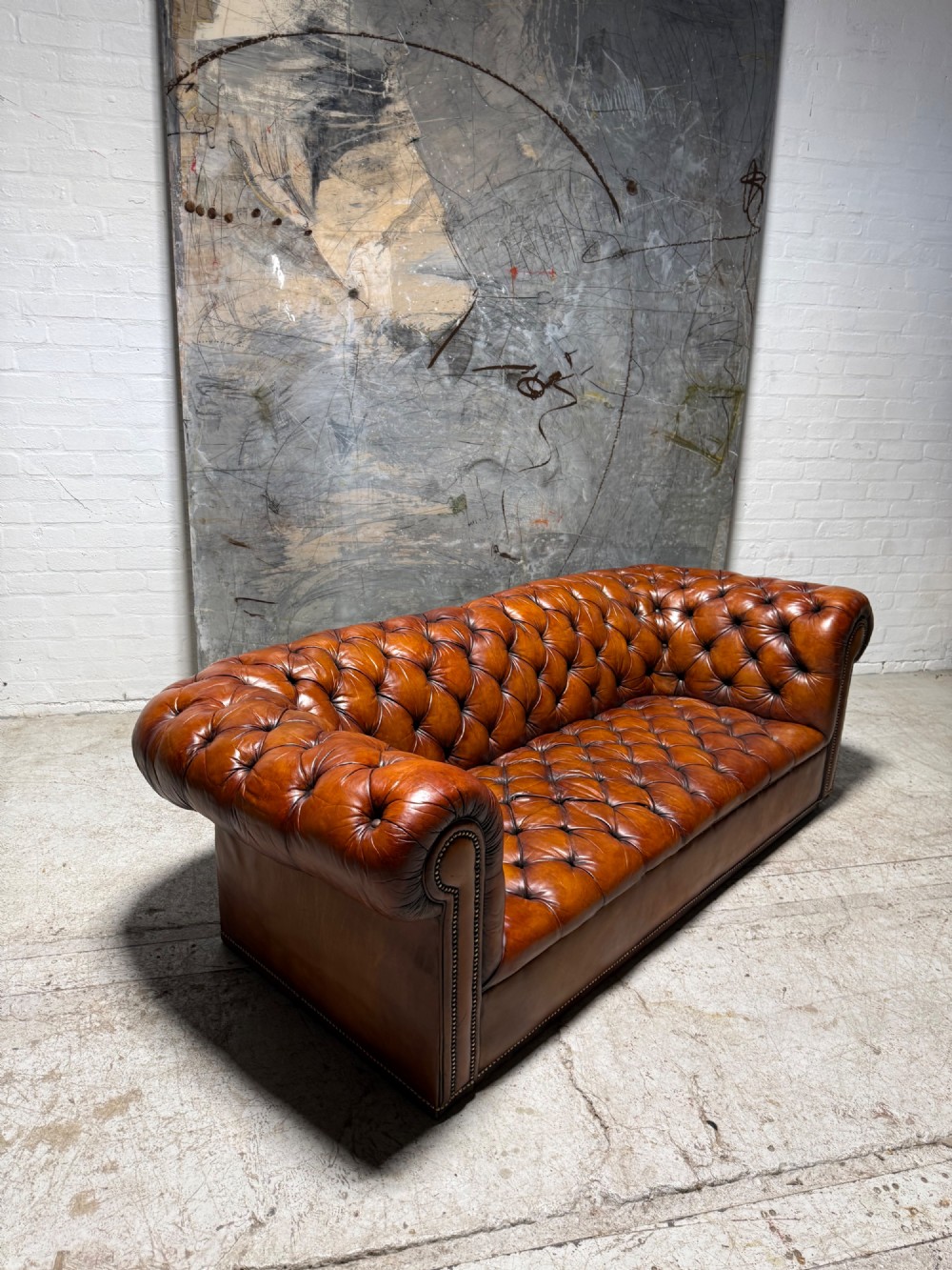 An early twentieth-century three-seater leather Chesterfield sofa with deep-buttoned tufted upholstery, rolled arms, and brass studding detail. View IV