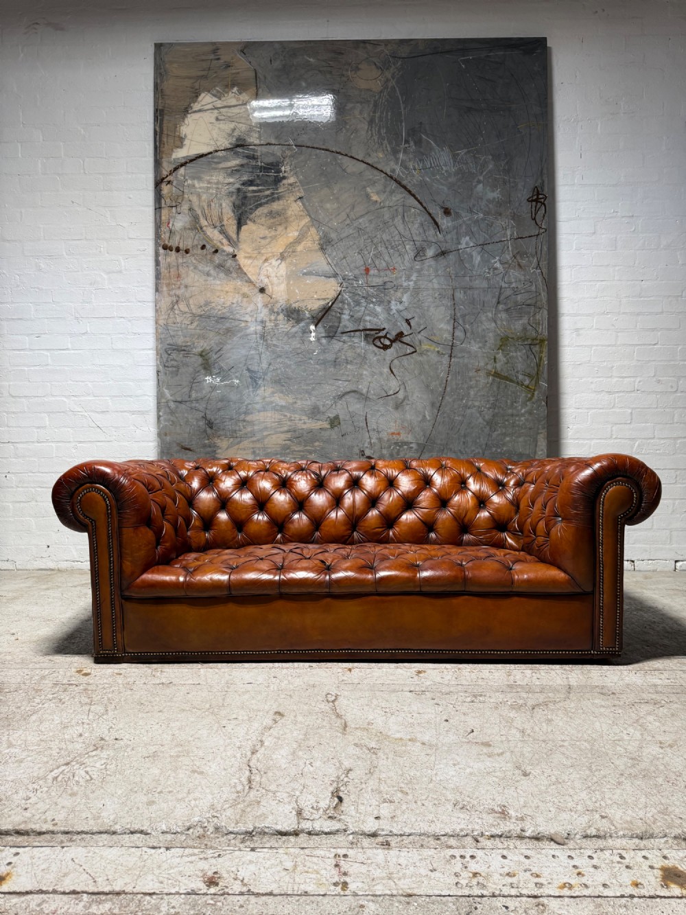 An early twentieth-century three-seater leather Chesterfield sofa with deep-buttoned tufted upholstery, rolled arms, and brass studding detail. View V