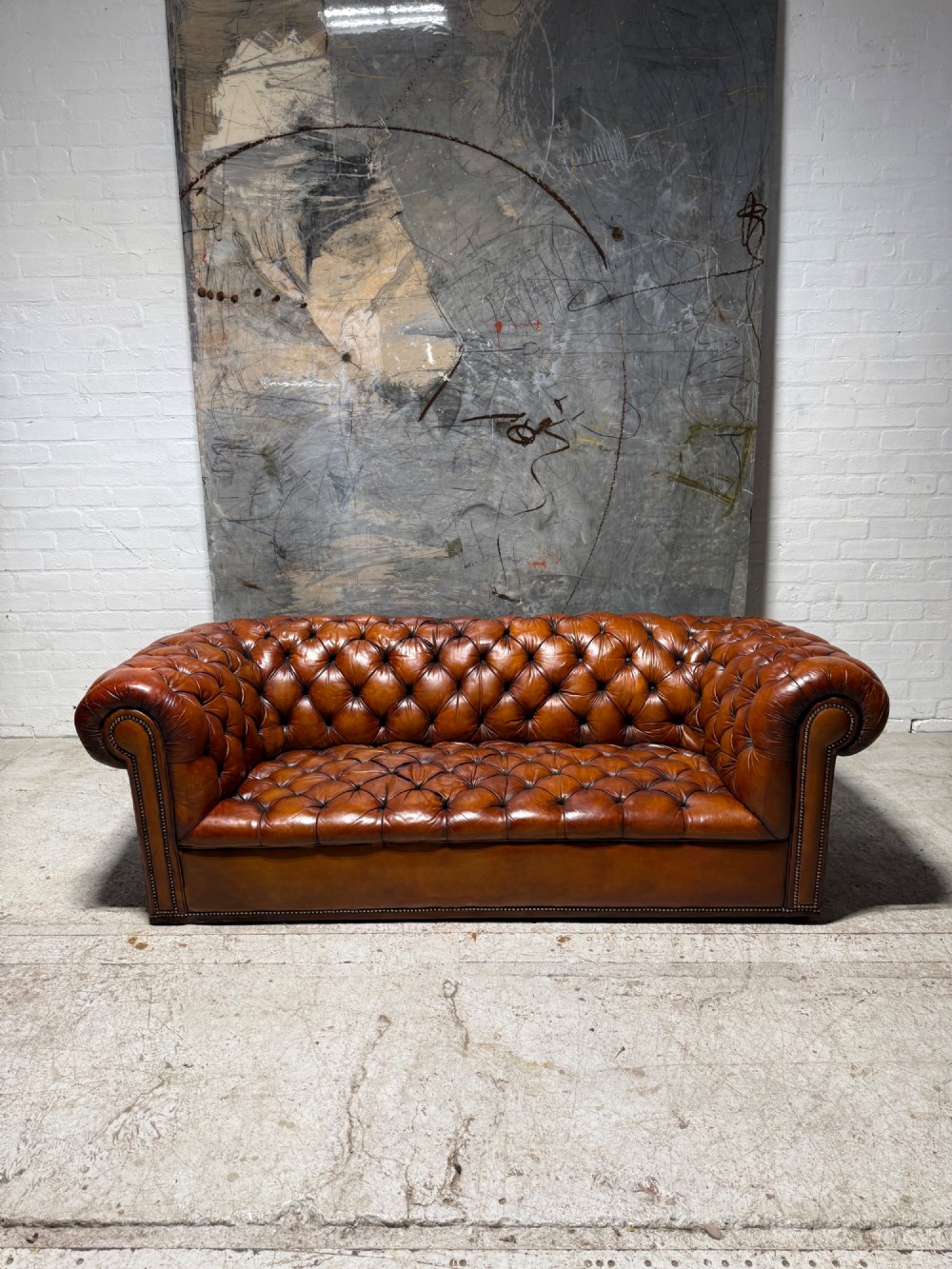 An early twentieth-century three-seater leather Chesterfield sofa with deep-buttoned tufted upholstery, rolled arms, and brass studding detail. View VI