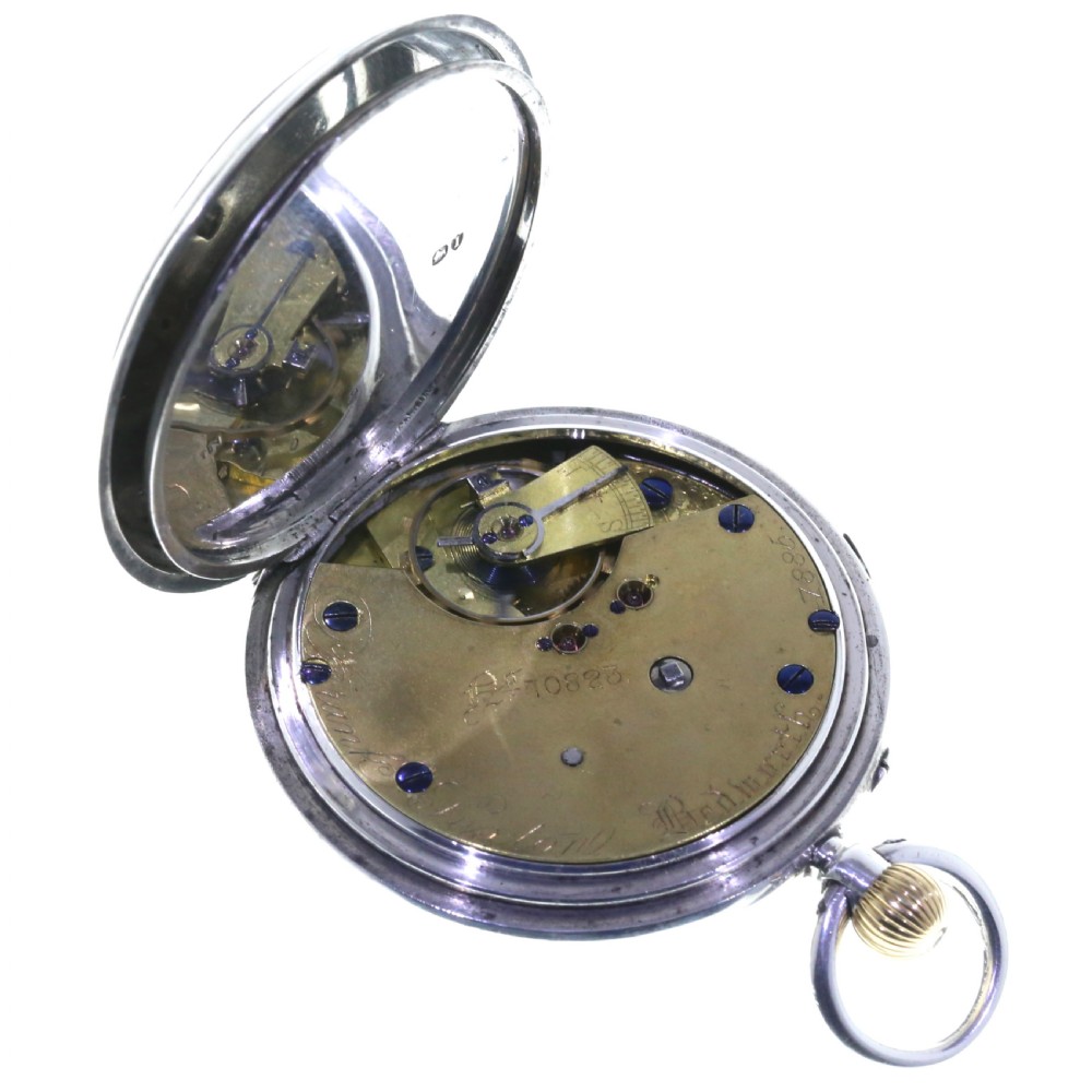 An antique silver open-face chronograph pocket watch featuring a white enamel dial with black Roman numerals and a brass winding crown. View V