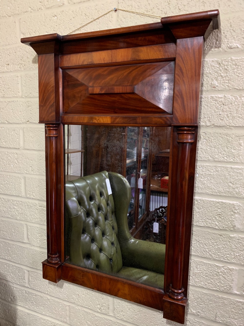 A rectangular antique mahogany wall mirror featuring a projected upper cornice, a faceted flame mahogany top panel, and side columns.