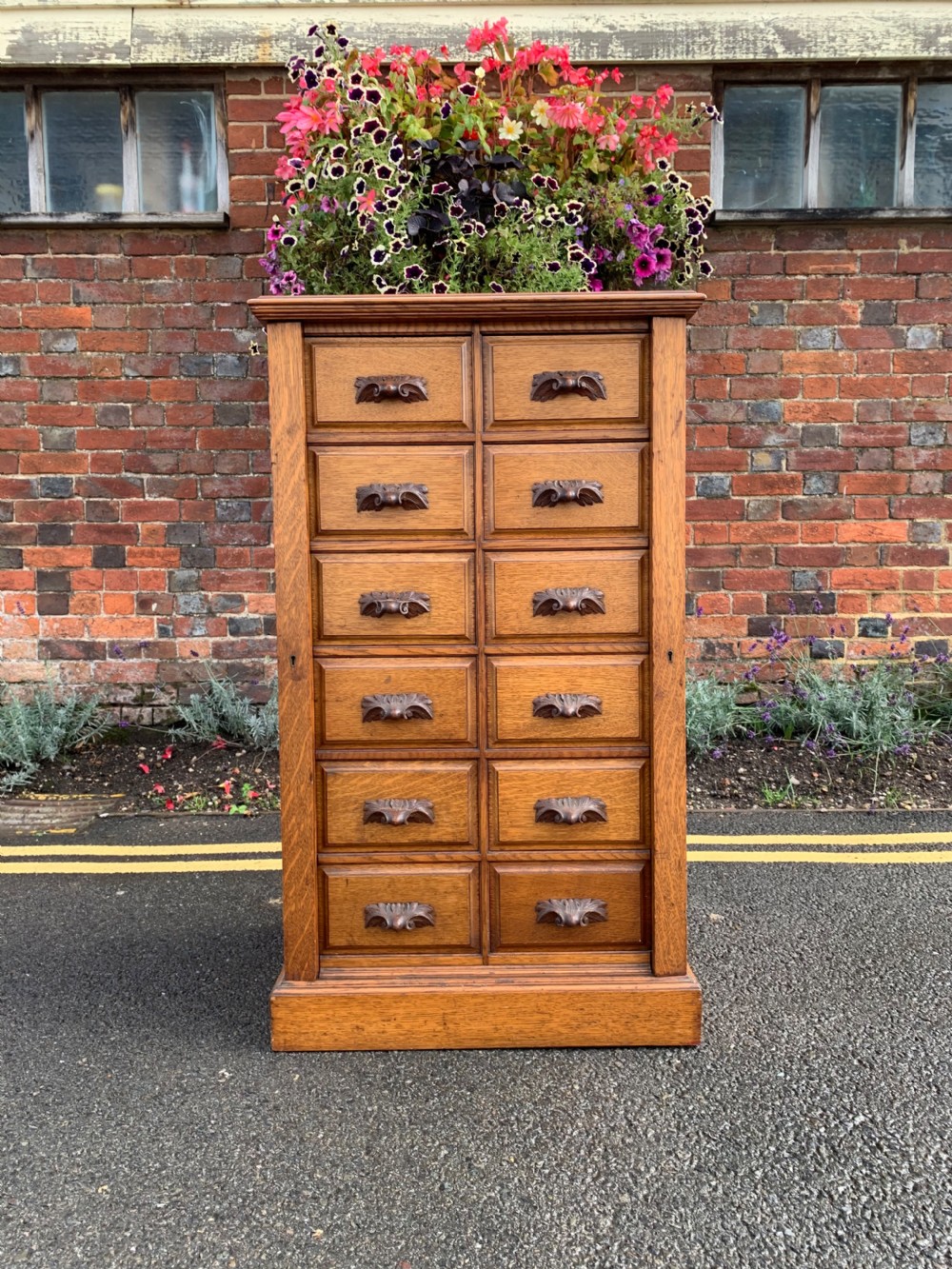 A tall Victorian oak Wellington chest featuring twelve drawers arranged in two columns with carved wooden pulls set on a solid plinth base.