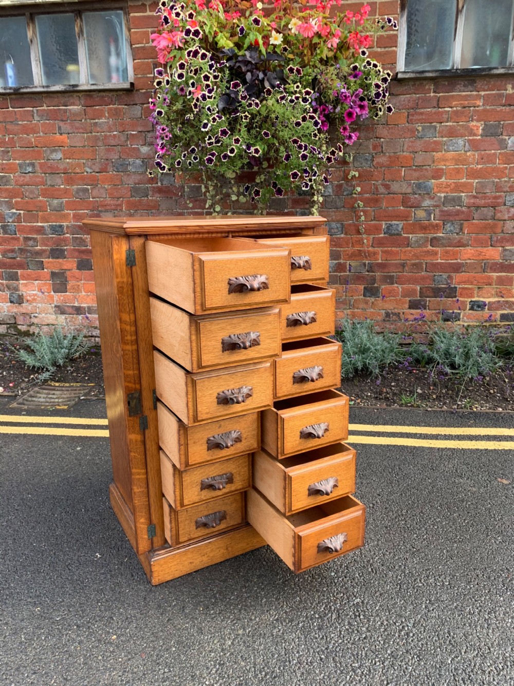 A tall Victorian oak Wellington chest featuring twelve drawers arranged in two columns with carved wooden pulls set on a solid plinth base. View III