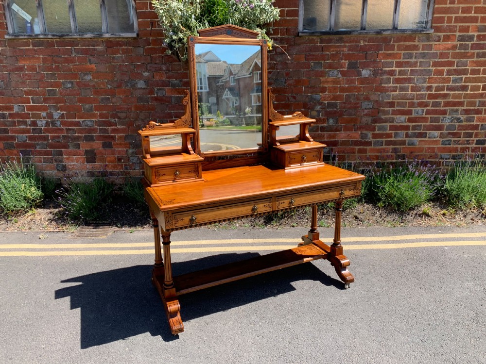 An Aesthetic Movement wooden dressing table featuring a central adjustable mirror, elevated trinket drawers, incised floral carvings, and turned legs on castors.