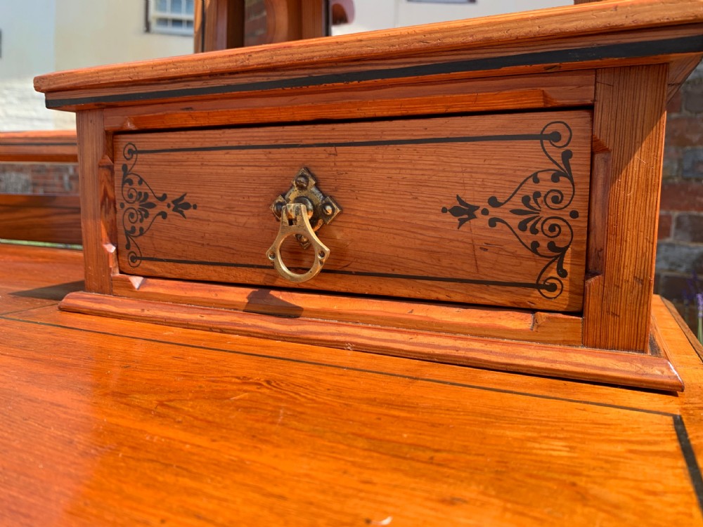 An Aesthetic Movement wooden dressing table featuring a central adjustable mirror, elevated trinket drawers, incised floral carvings, and turned legs on castors. View III