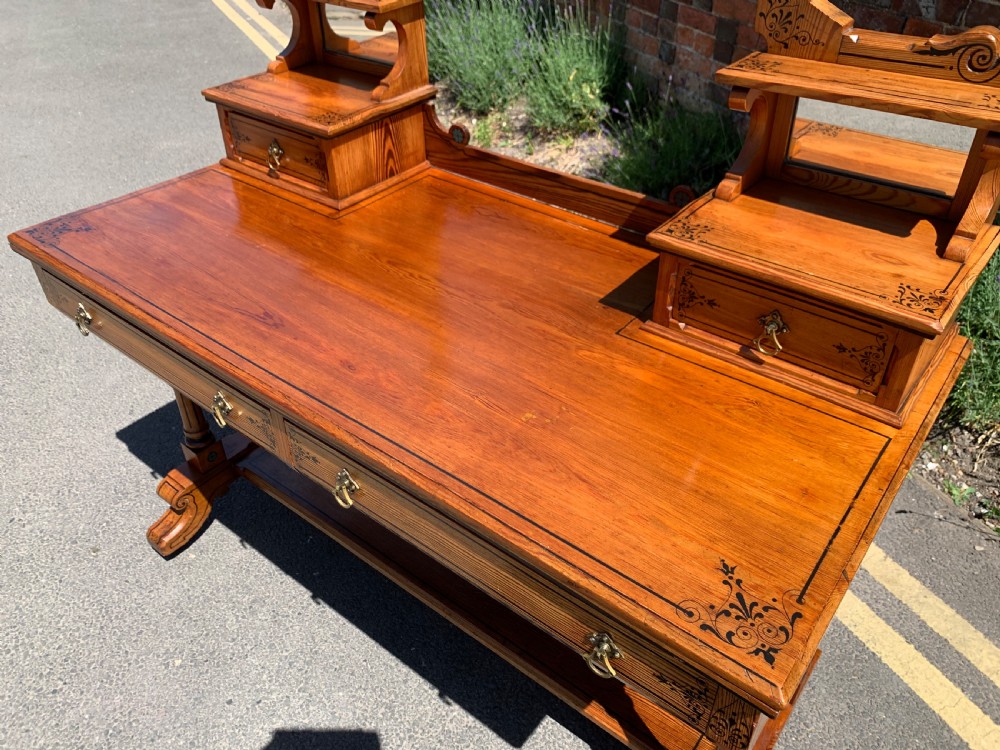 An Aesthetic Movement wooden dressing table featuring a central adjustable mirror, elevated trinket drawers, incised floral carvings, and turned legs on castors. View XI