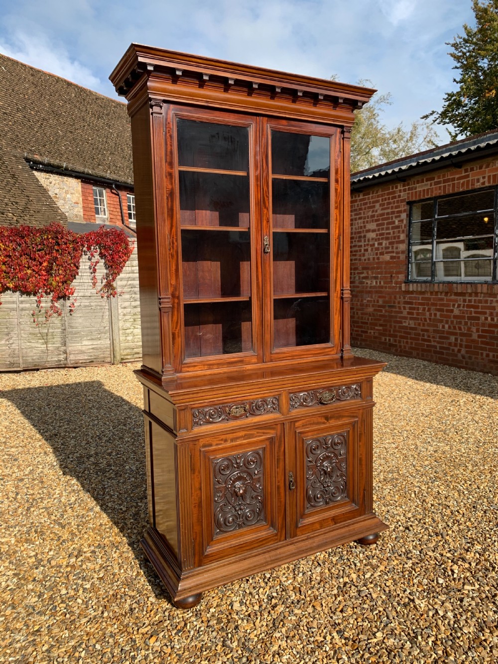 A tall Victorian mahogany bookcase with two upper glazed doors, two carved drawers, and lower carved cupboard doors.
