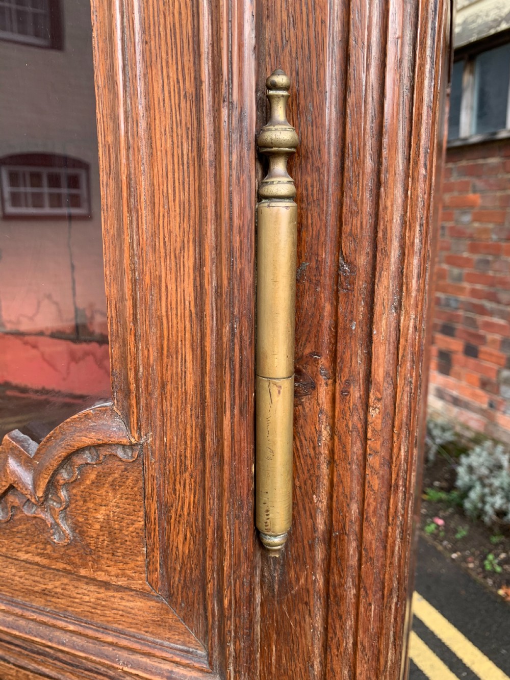 A tall, narrow antique oak cabinet with a glazed upper door, central carved drawers, and a lower panelled cupboard door. View III