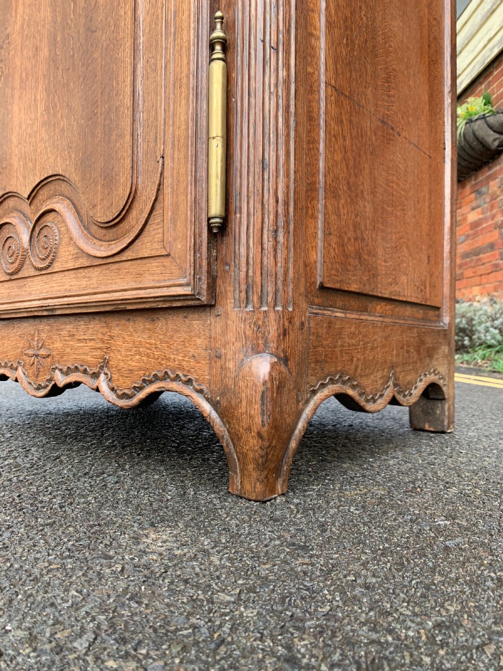 A tall, narrow antique oak cabinet with a glazed upper door, central carved drawers, and a lower panelled cupboard door. View V