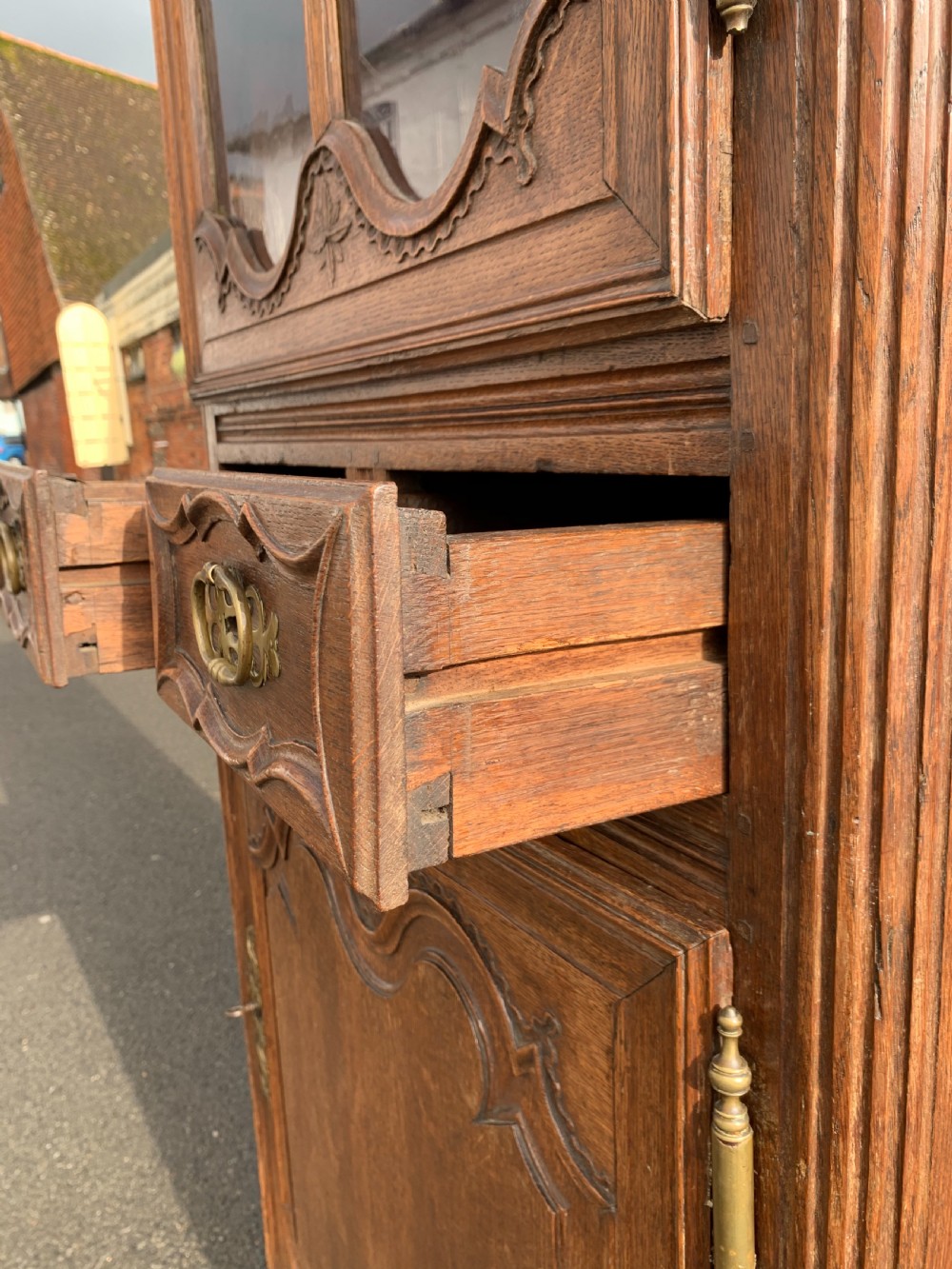 A tall, narrow antique oak cabinet with a glazed upper door, central carved drawers, and a lower panelled cupboard door. View VIII
