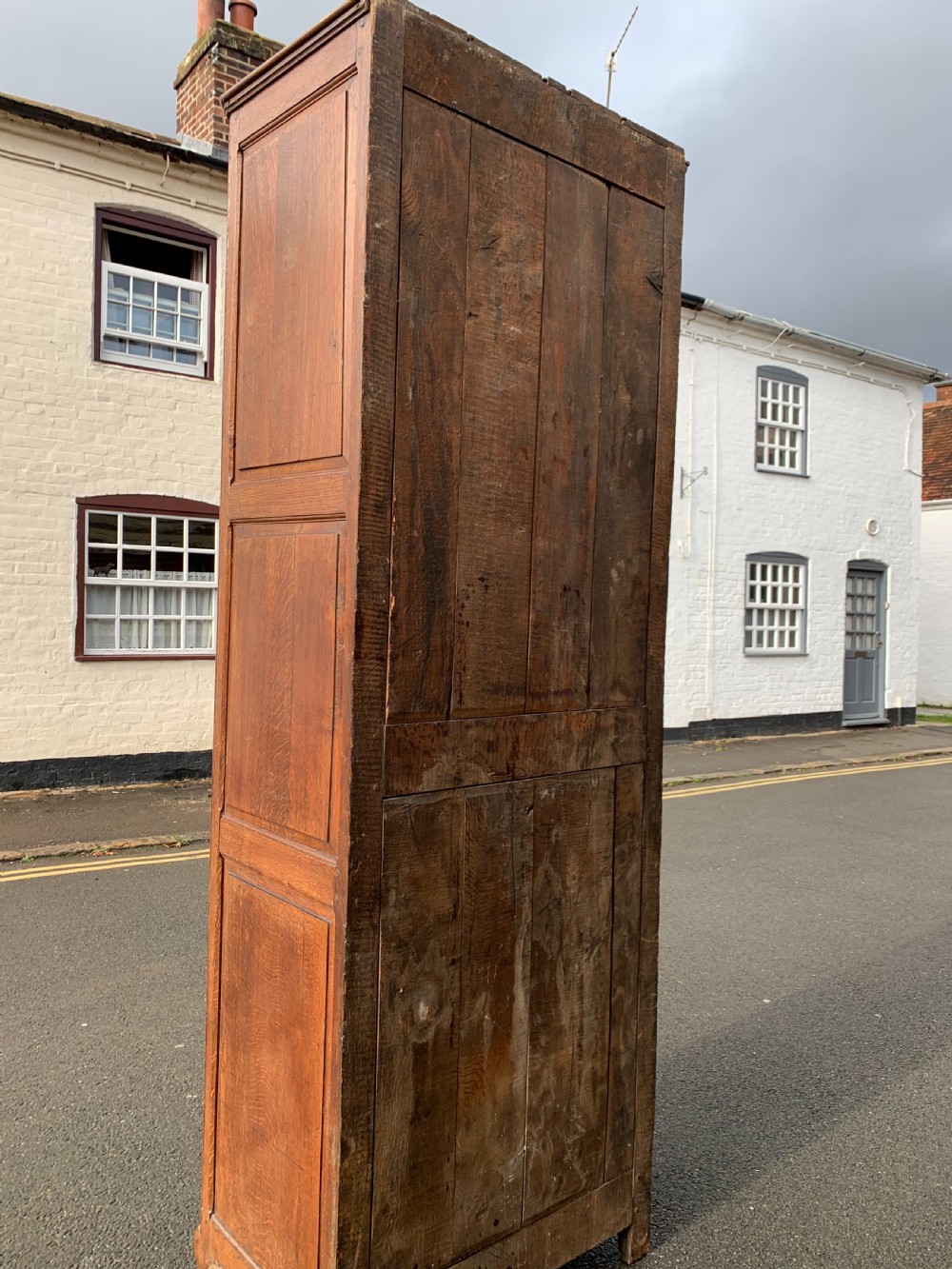 A tall, narrow antique oak cabinet with a glazed upper door, central carved drawers, and a lower panelled cupboard door. View IX
