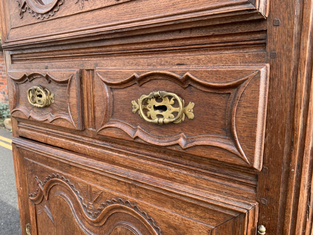 A tall, narrow antique oak cabinet with a glazed upper door, central carved drawers, and a lower panelled cupboard door. View X
