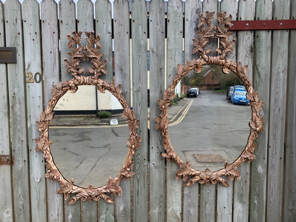 A pair of oval wall mirrors featuring ornate carved wooden frames with oak leaf motifs and ribbon crests in a painted finish.