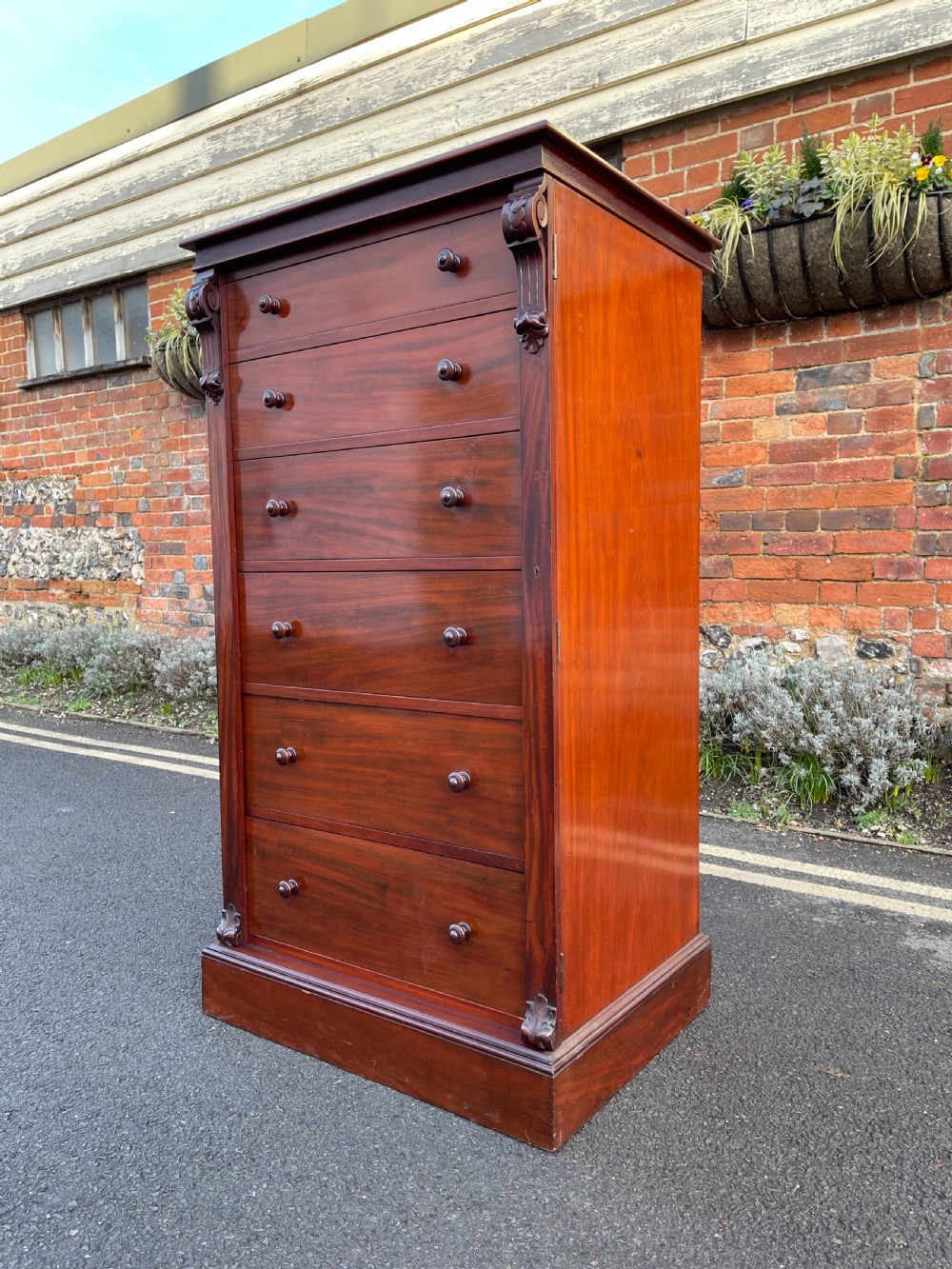 A tall Victorian mahogany Wellington chest featuring seven graduated drawers with turned wooden knobs, carved side corbels, and a side locking pilaster.