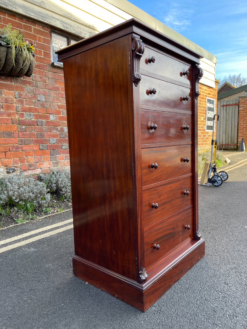 A tall Victorian mahogany Wellington chest featuring seven graduated drawers with turned wooden knobs, carved side corbels, and a side locking pilaster. View X