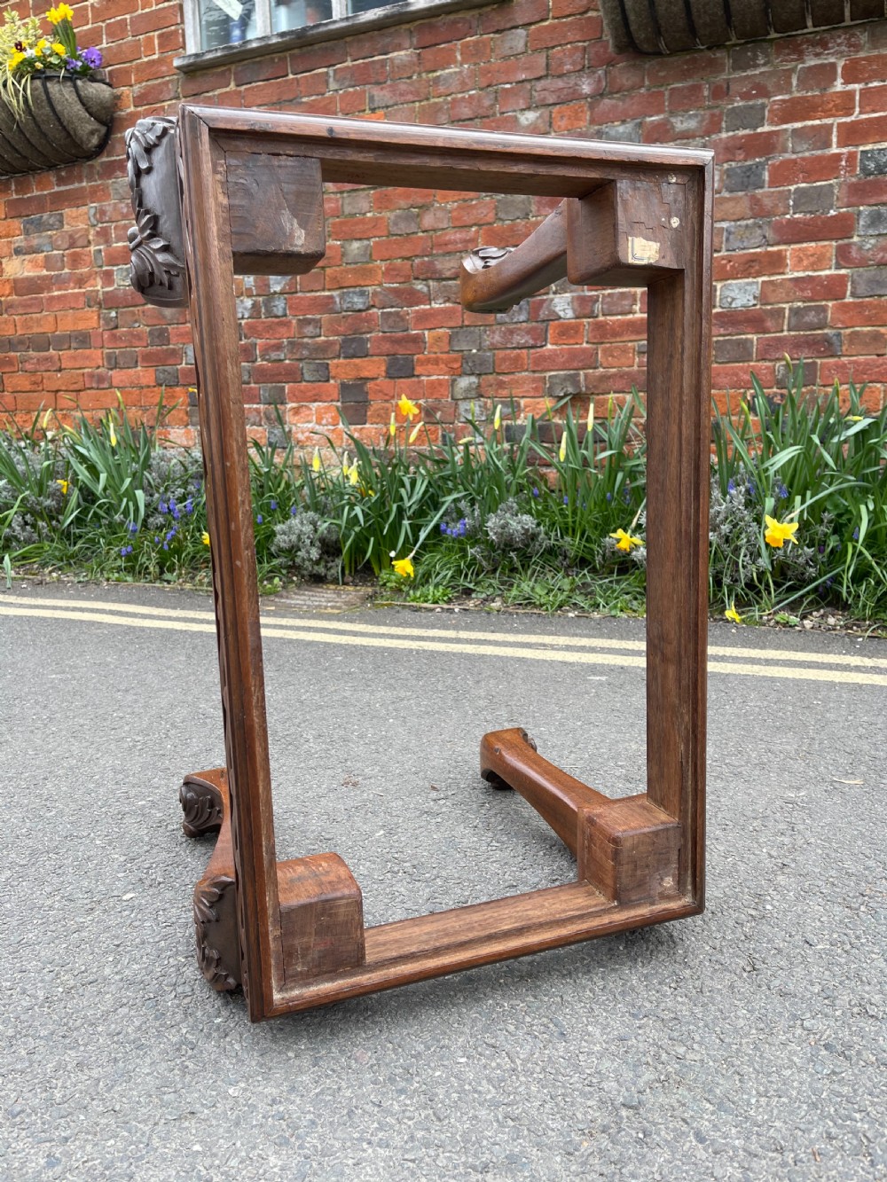 A carved teak Anglo-Indian stool featuring ornate cabriole legs, a decorative carved apron, and a red damask upholstered top. View V