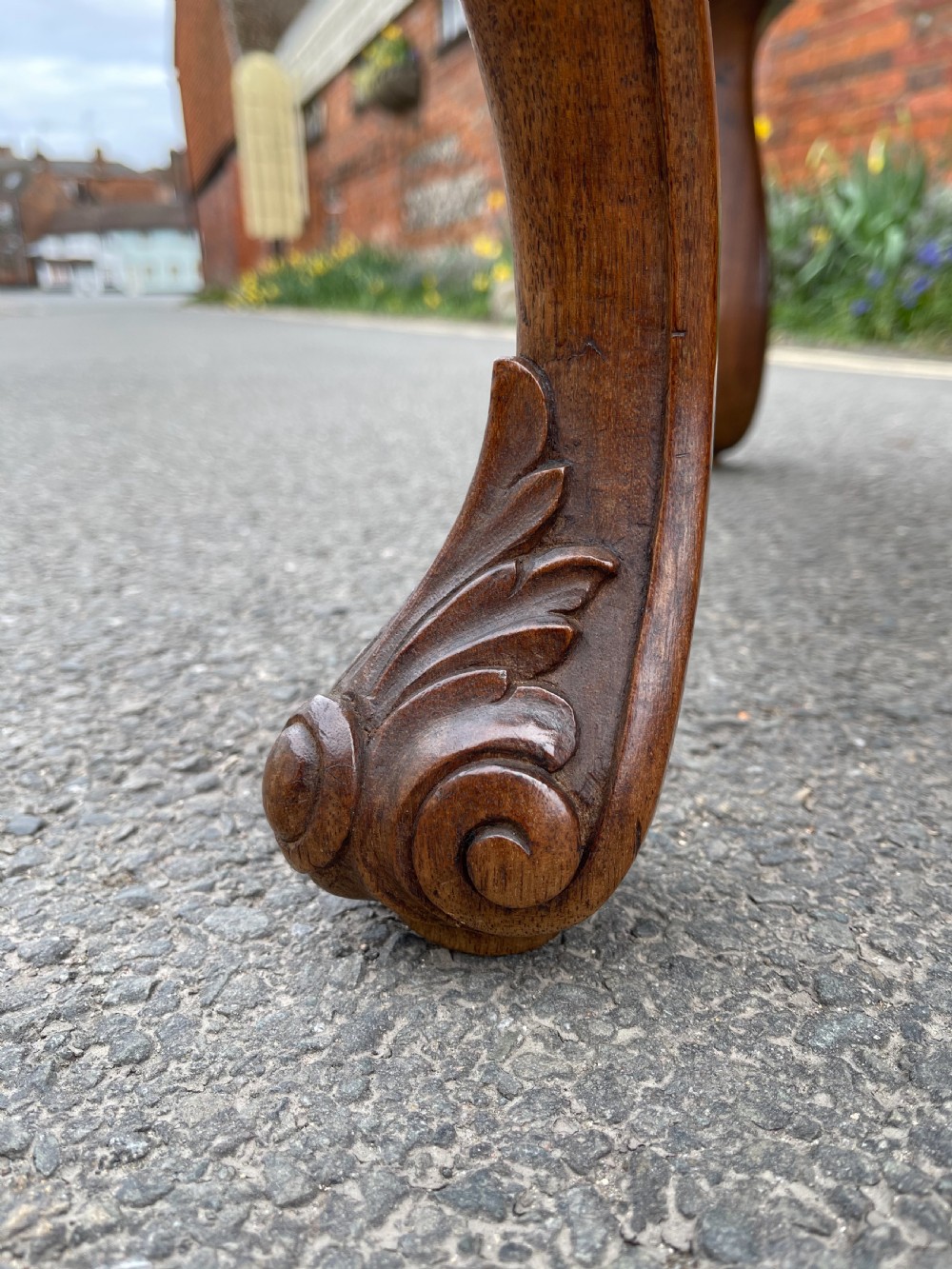 A carved teak Anglo-Indian stool featuring ornate cabriole legs, a decorative carved apron, and a red damask upholstered top. View VI