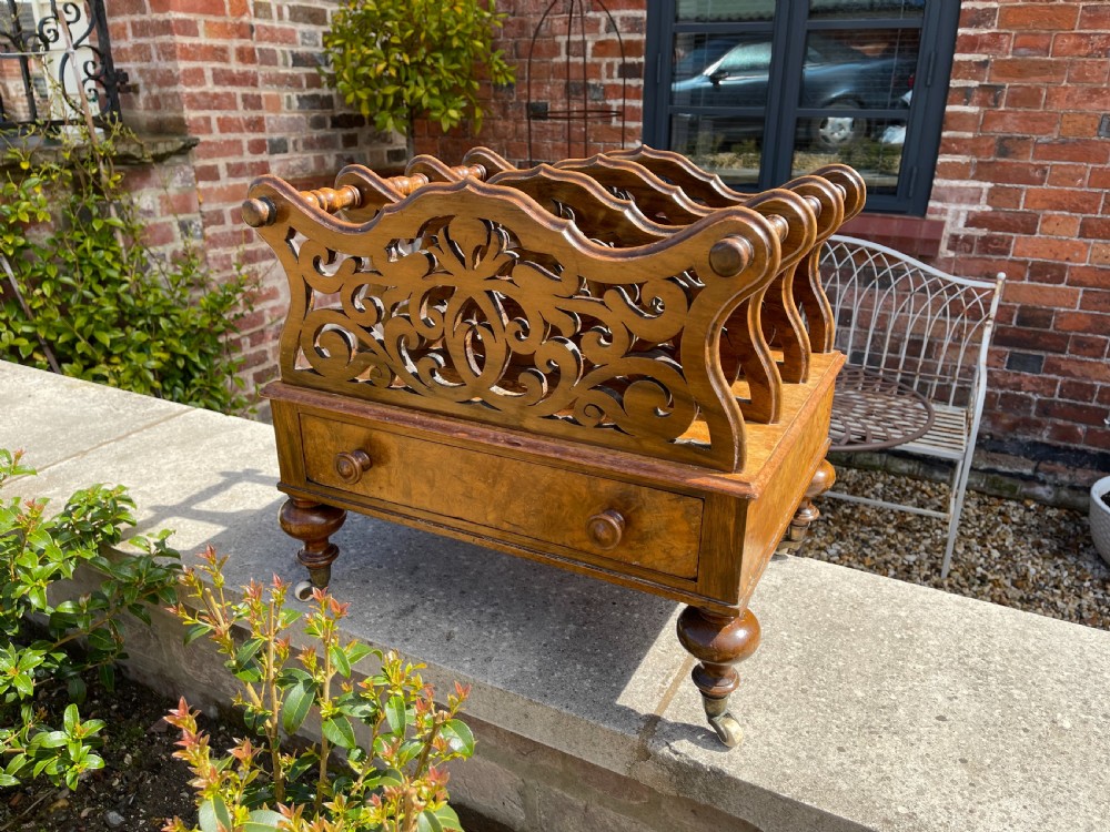 A Victorian figured walnut music Canterbury with pierced fretwork dividers, a single base drawer with turned wooden knobs, and turned legs on castors.