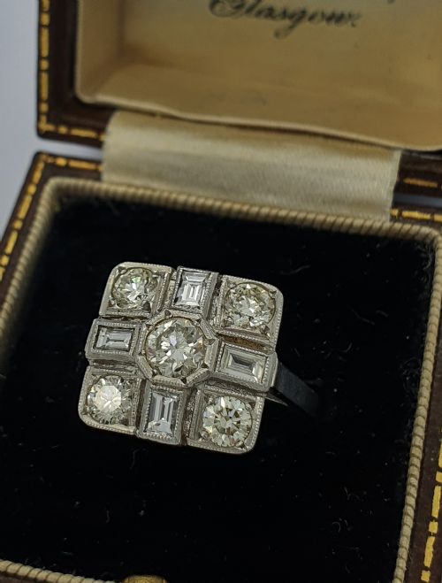 fig 2. An Art Deco platinum cocktail ring featuring a geometric rectangular plaque setting filled with round and rectangular diamonds and detailed millegrain edging.