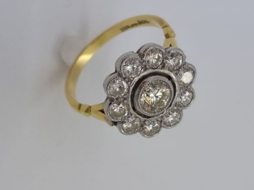 fig 1. An antique diamond cluster ring featuring a central round diamond encircled by ten smaller diamonds set in a white metal head with a yellow gold band.