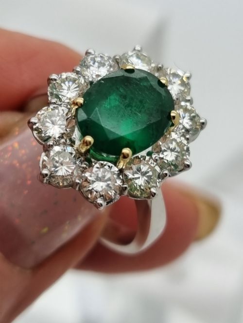 fig 1. An 18ct gold ring featuring a central oval green emerald framed by a halo of round brilliant-cut diamonds.