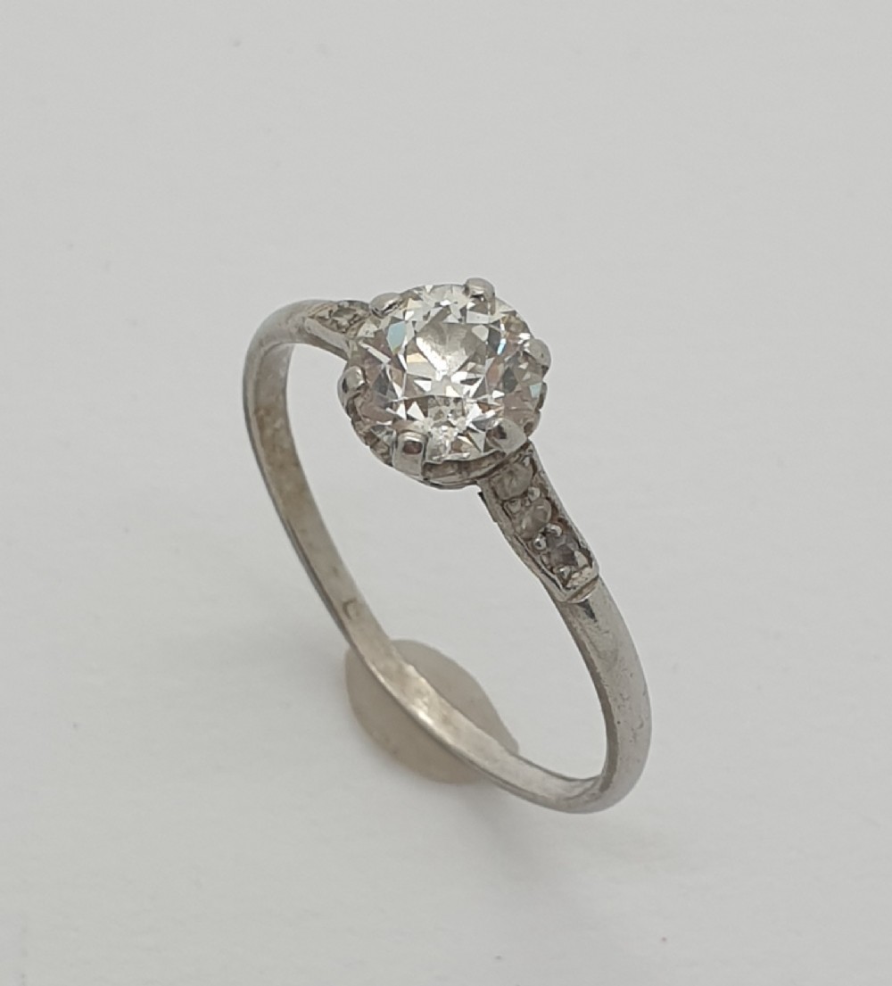 A silver-toned diamond solitaire ring featuring a round brilliant cut central diamond held in a claw setting with small accent diamonds on the shoulders.
