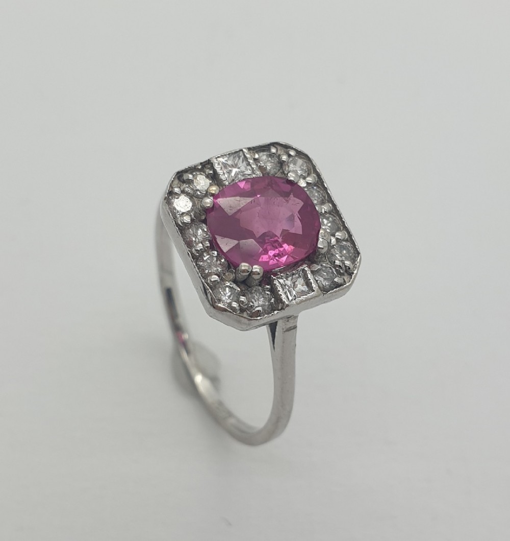 An 18ct white gold ring featuring a central oval pink sapphire set within a geometric square cluster of brilliant and princess cut diamonds.