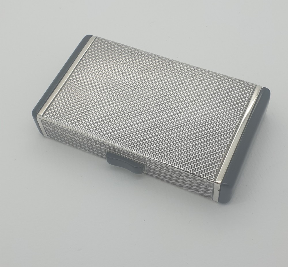 An Art Deco rectangular sterling silver case featuring an engine-turned geometric pattern and black enamelled end caps.