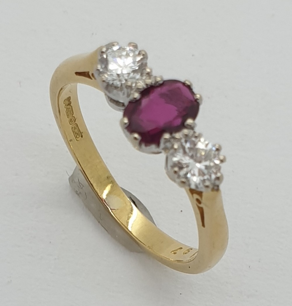 An 18ct yellow gold trilogy ring with a central oval cut red ruby flanked by two brilliant cut diamonds.