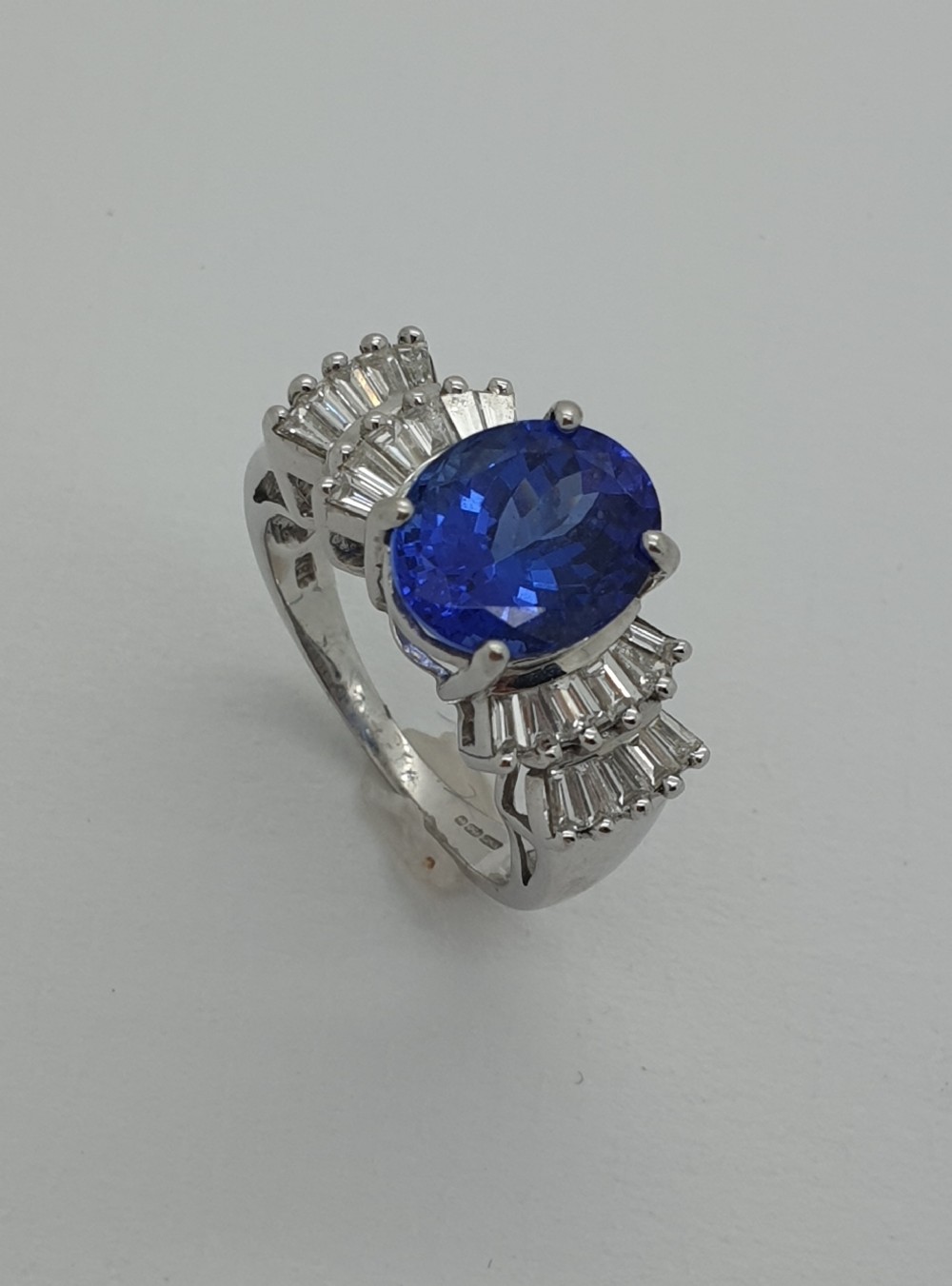 An oval-cut blue-violet tanzanite ring set in white gold with tiered baguette diamond shoulders.