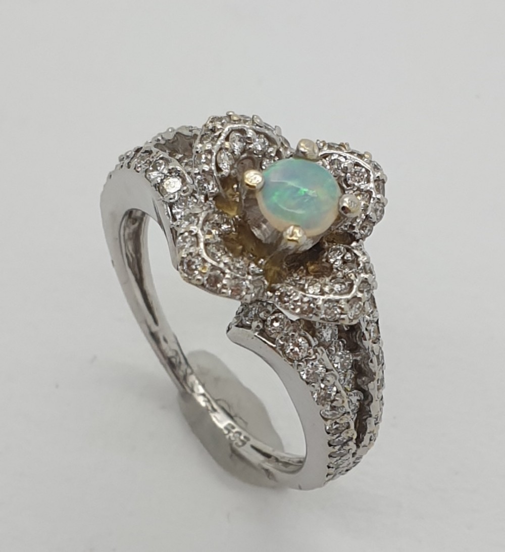 A white gold floral cluster ring featuring a central round opal cabochon surrounded by multi-tiered petals set with pave diamonds.