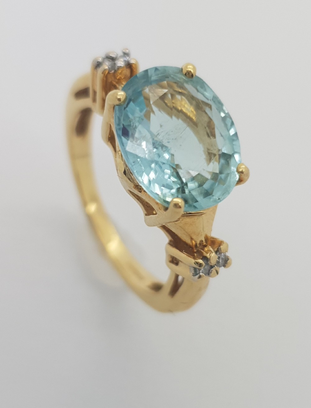 An 18ct yellow gold ring set with an oval light blue aquamarine flanked by small claw-set diamond accents on the shoulders.