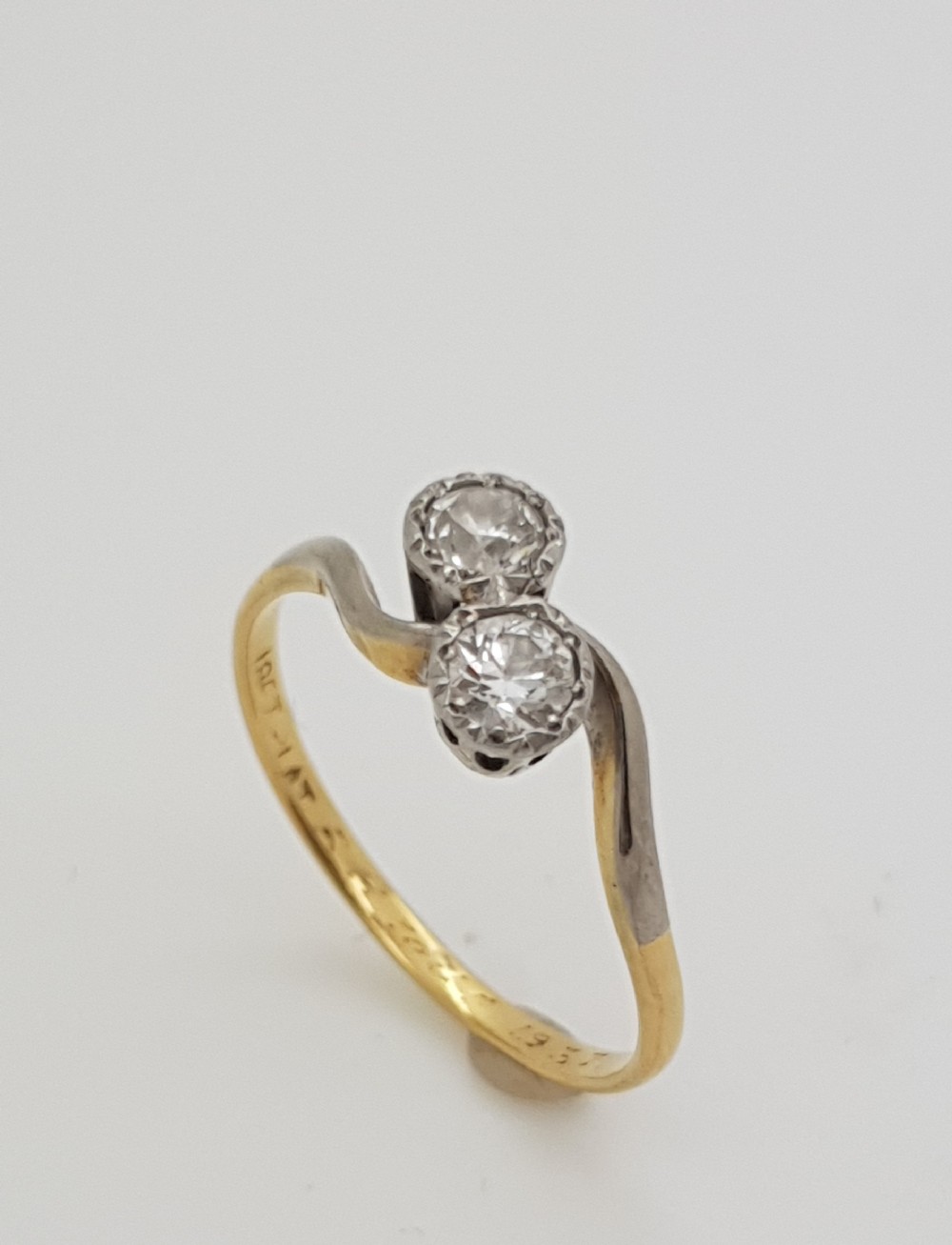 An 18ct yellow gold and platinum crossover ring with two round diamonds set in a diagonal twist arrangement.