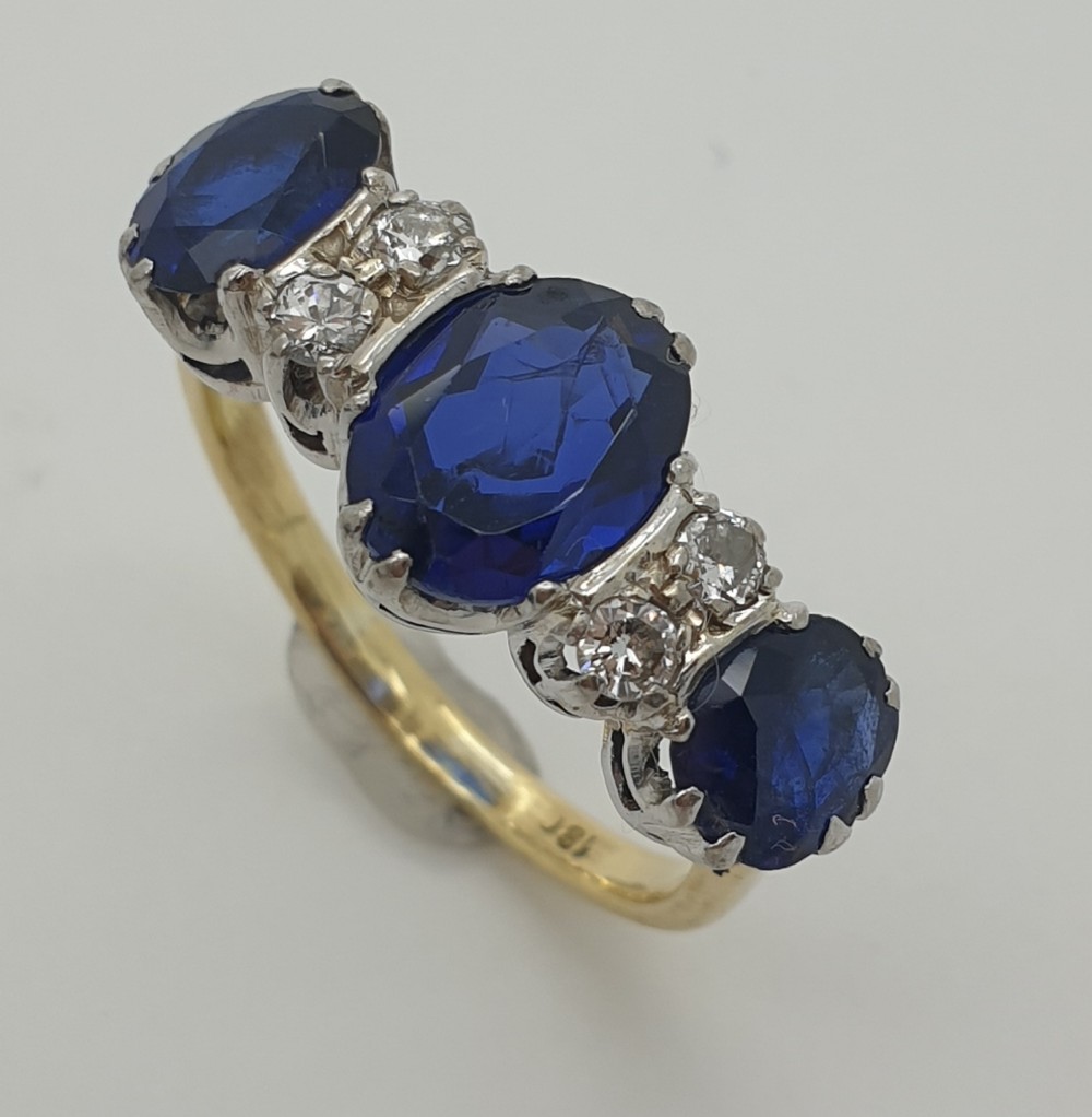 A yellow gold three-stone ring featuring three oval blue sapphires separated by pairs of small round diamonds.