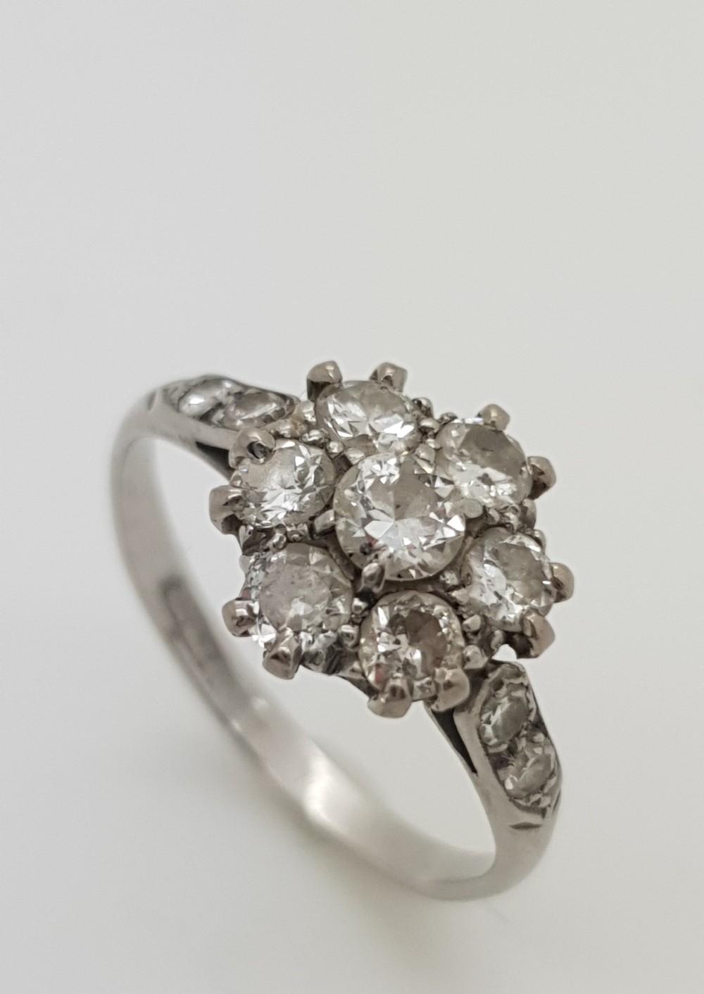 A platinum ring featuring a central round brilliant cut diamond framed by a cluster of seven smaller round diamonds with diamond-set shoulders.