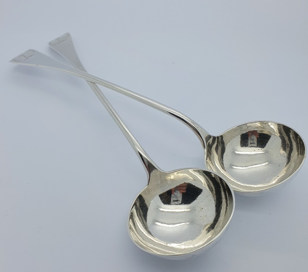 A pair of Georgian sterling silver toddy ladles with round bowls and long flared handles positioned crossed over each other.