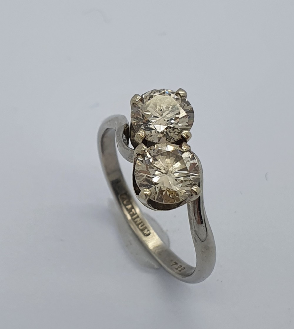 A platinum ring featuring two claw-set round brilliant diamonds in a curved crossover twist band.