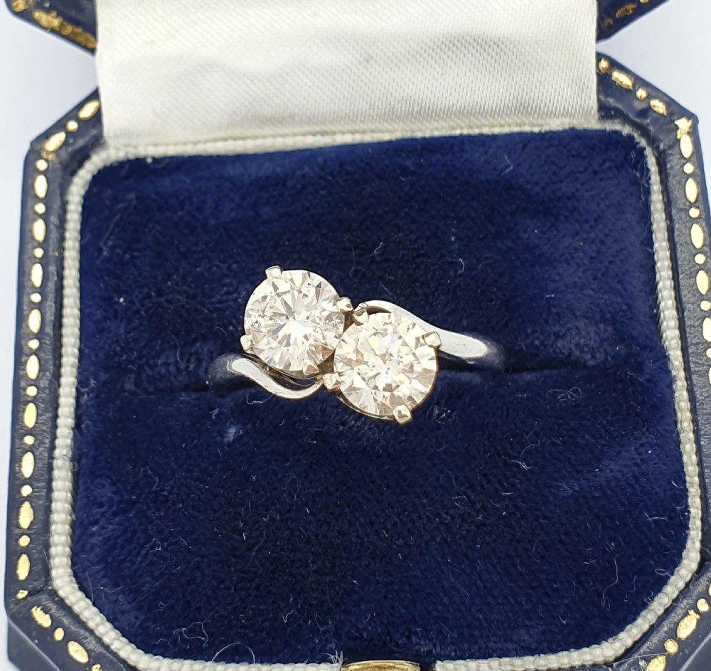A platinum ring featuring two claw-set round brilliant diamonds in a curved crossover twist band. View IV