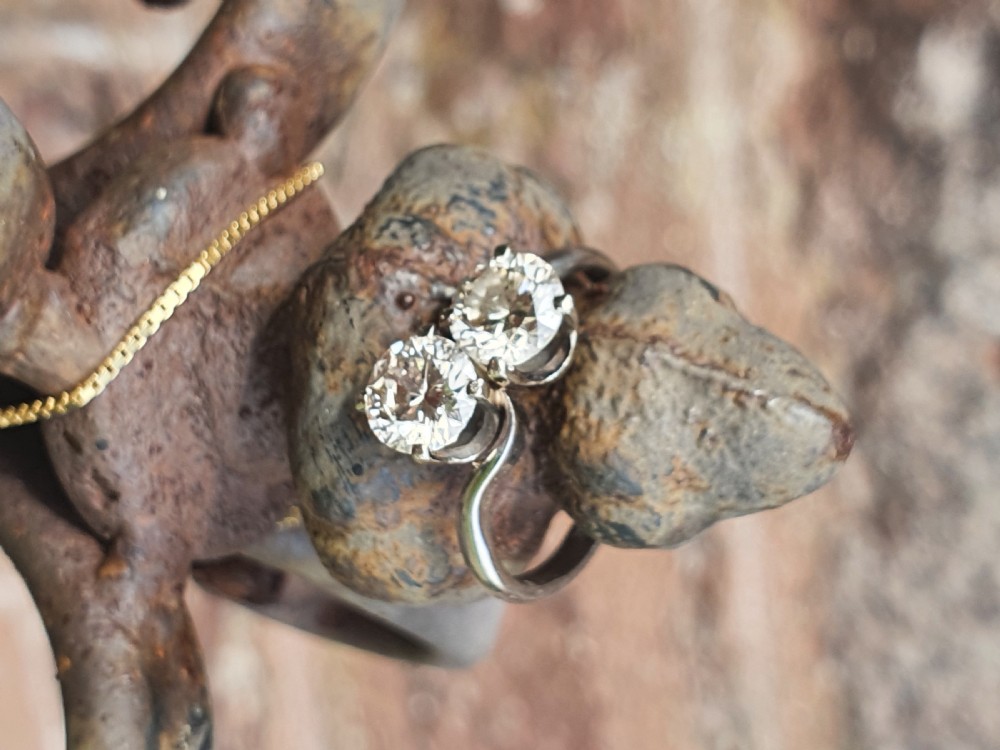 A platinum ring featuring two claw-set round brilliant diamonds in a curved crossover twist band. View VIII