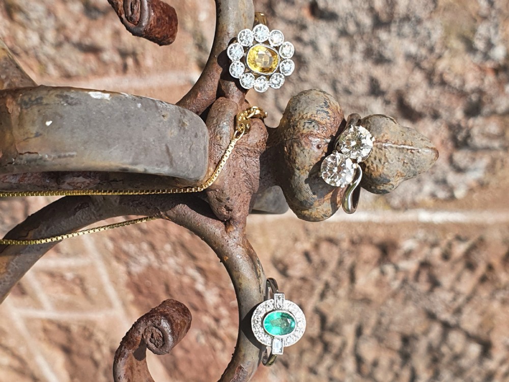 An Art Deco style white metal ring featuring a central oval green emerald within a circular diamond halo accented by baguette-cut side diamonds. View VIII