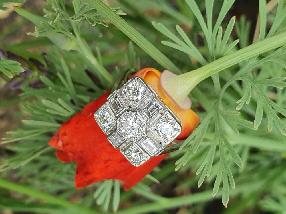 An Art Deco platinum cocktail ring featuring a geometric rectangular plaque setting filled with round and rectangular diamonds and detailed millegrain edging.