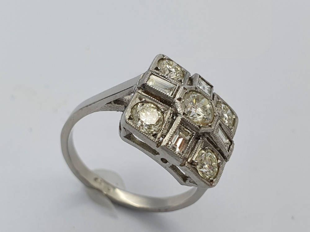 An Art Deco platinum cocktail ring featuring a geometric rectangular plaque setting filled with round and rectangular diamonds and detailed millegrain edging. View VI