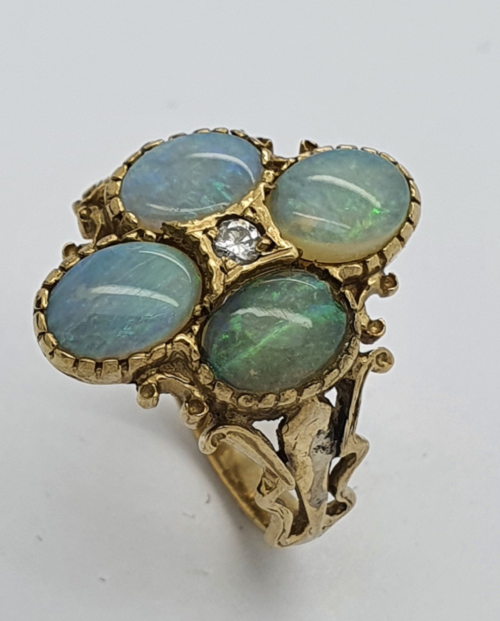 A 9ct yellow gold dress ring featuring four oval cabochon opals arranged in a cluster around a central brilliant-cut diamond, mounted on an ornate scrollwork band.